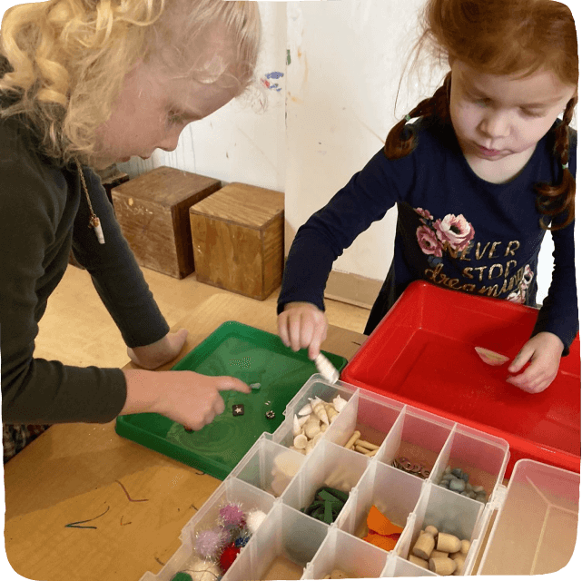 Two girls looking through tray of loose parts