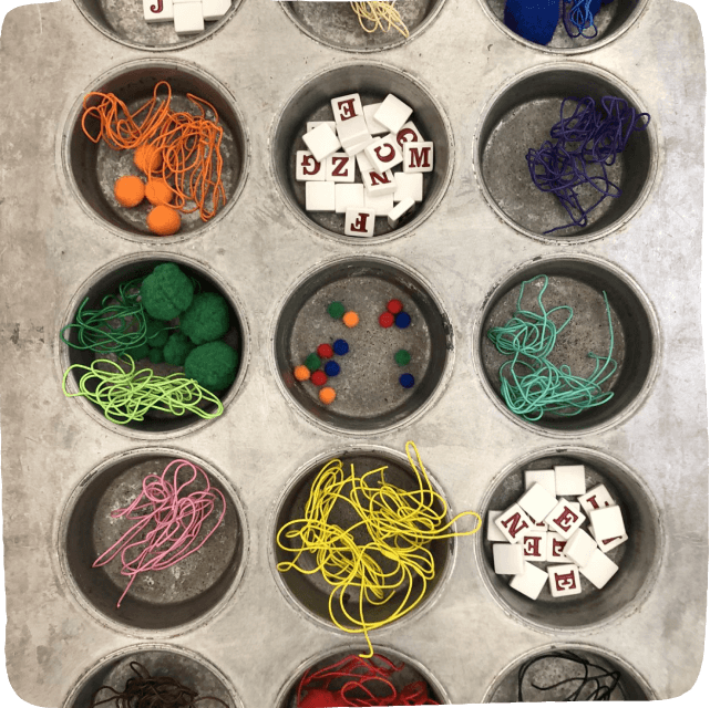 Image of a muffin tin filled with loose parts such as wires, pompoms, and scrabble tiles.