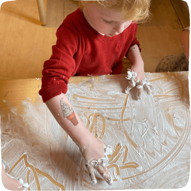 little boy making marks in shaving cream on a tabletop