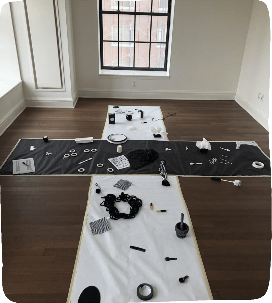 Image of a play-based learning activity set up featuring black & white  materials such as ropes, spoons, rings, boxes, and other household items atop black and white butcher paper. 