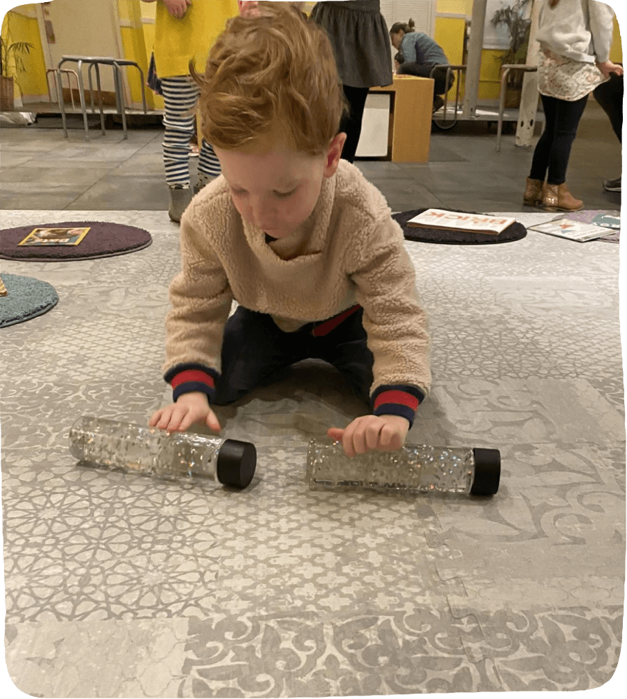 Image of a child engaging in a social emotional learning activity: rolling sensory bottles filled with water and glitter on a play mat.