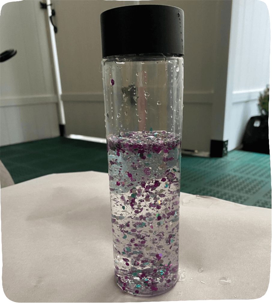 Image of the homemade sensory bottle created in this social emotional learning activity. This bottle is filled with water and purple & turquoise glitter.