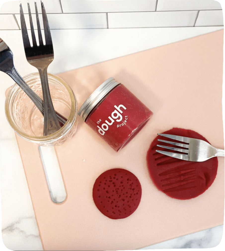 Image of a red blob of play-dough and a fork making imprints for use in this play-dough activity for kids.