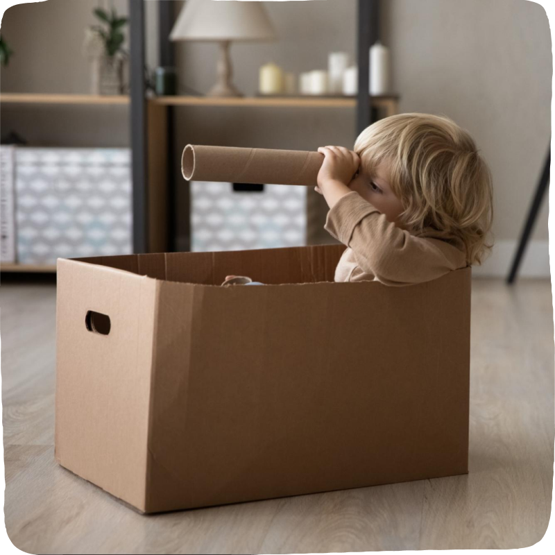 Little boy in a box pretending to sail a boat looking through a toilet paper roll like a spy glass