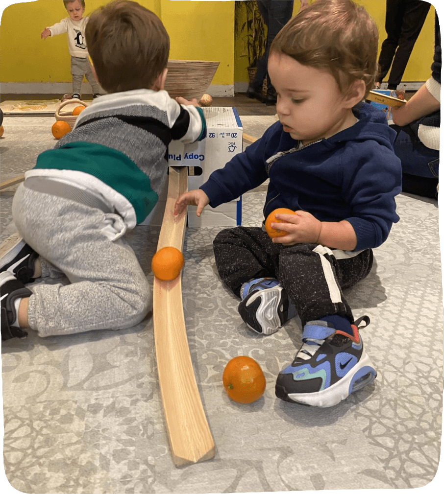Image of two small children rolling clementines down a ramp in this food activity for kids.