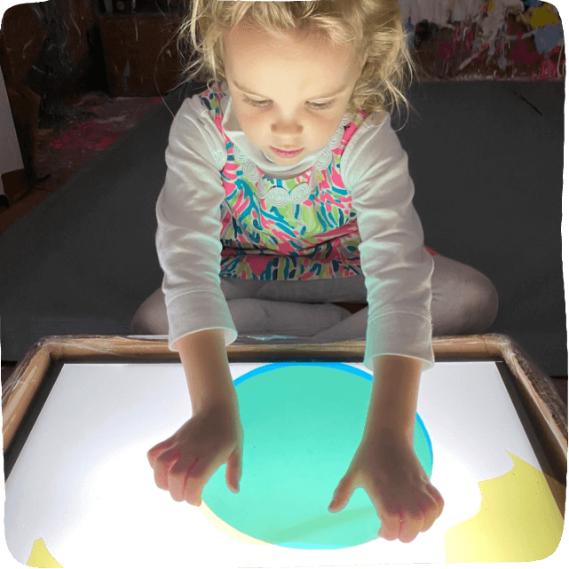 little girl with hands on a light table with acetate
