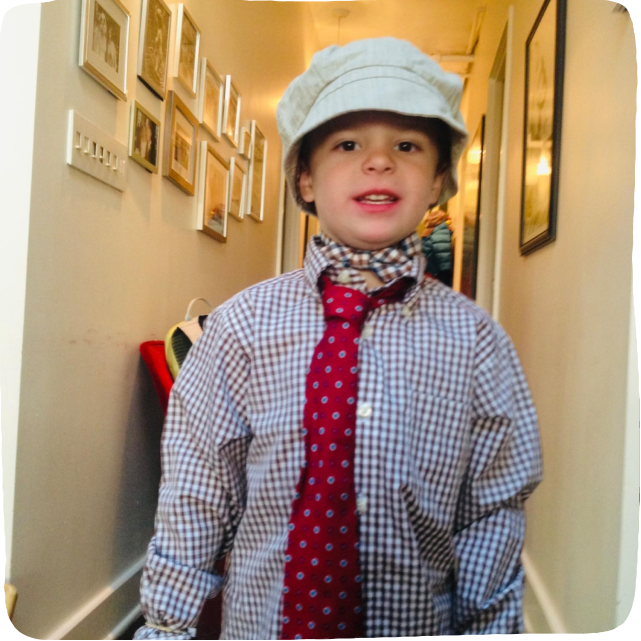 little boy in a hallway dressed in a grown up dress shirt, neck tie and funny hat