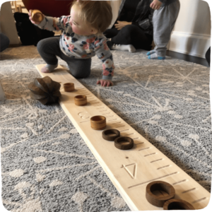 Baby crawling along a measuring stick with several wooden objects atop it. This is a perfect example of Line it Up play! 