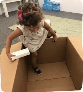 Little girl stepping inot an empty cardboad box.