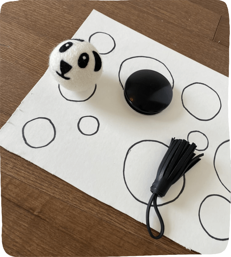 Image of black and white materials such as a dryer ball with a panda face atop a white piece of paper with black circles. A perfect set up for this play-based learning activity.