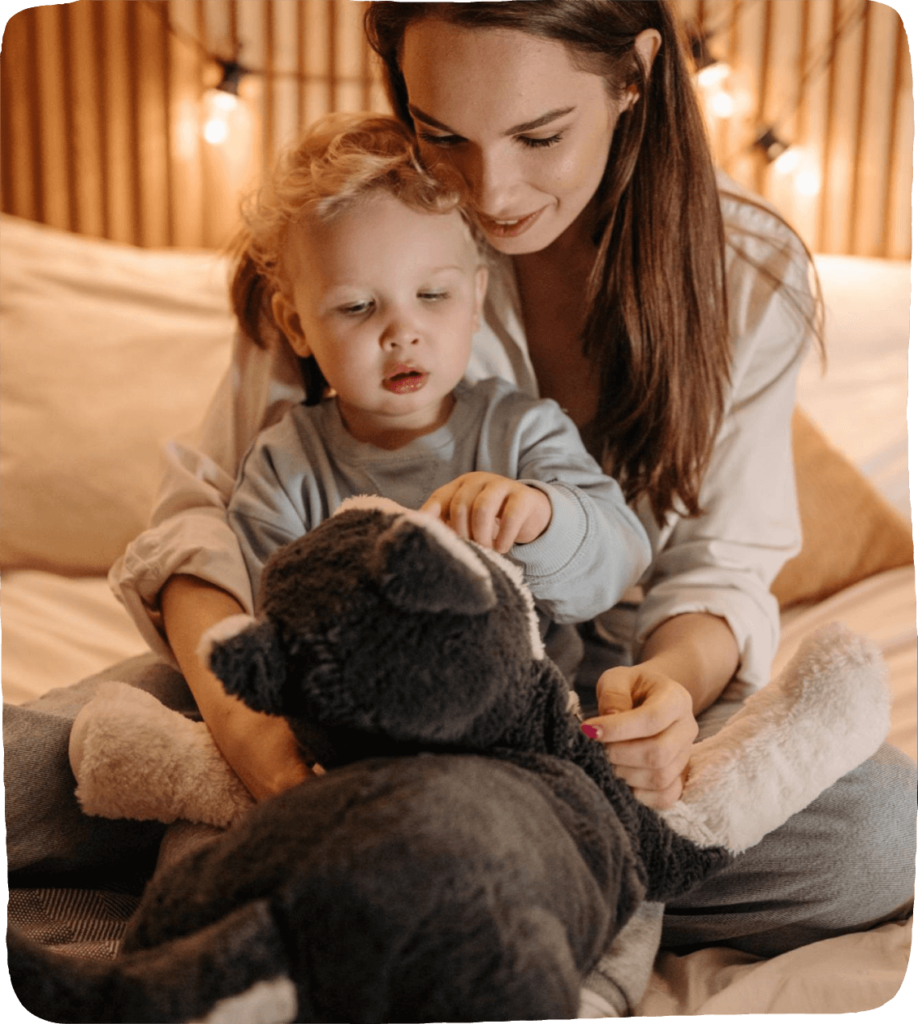 Image of a mother and child looking lovingly at a stuffed animal while snuggling on a bed. This is a suggested set-up for families to establish a safe foundation for social-emotional learning ideas.