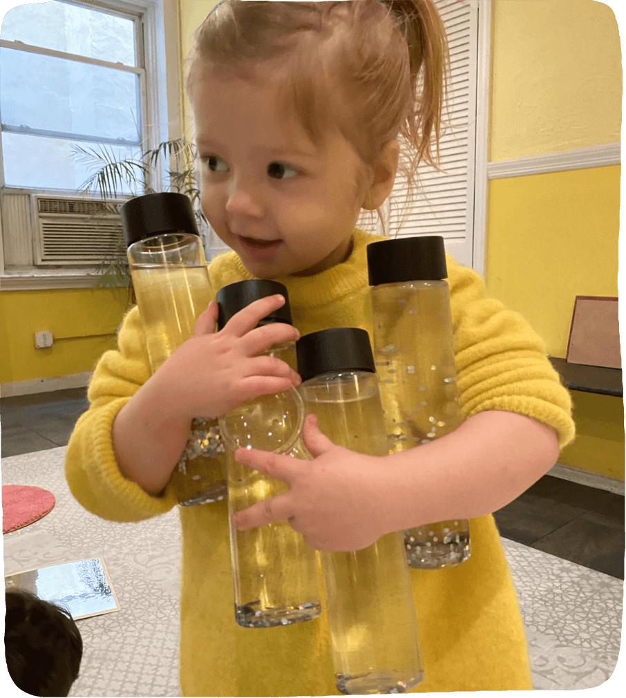 Image of a child holding an arm-full of homemade sensory bottles as part of this social emotional learning activity. 