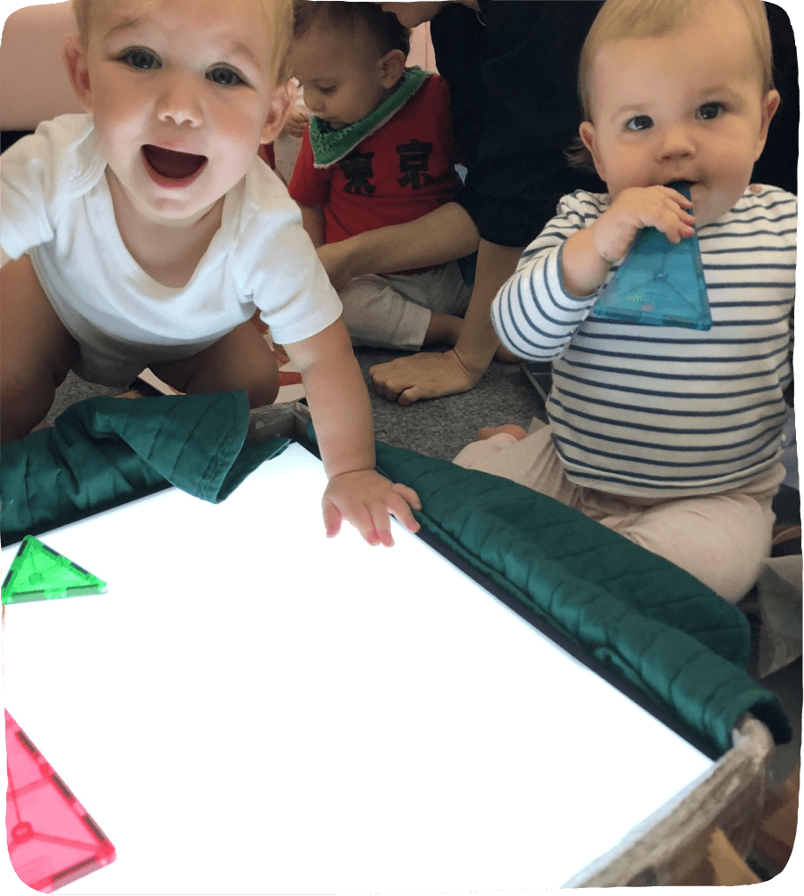An image of 1 year olds using Magnatiles on a DIY light table.