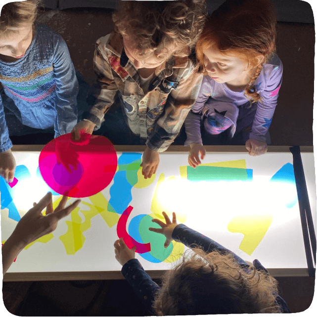 many children with hands on a light table with acetate