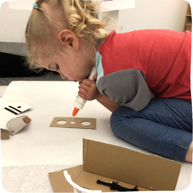 Image of a child engaging in the fun activity of building a house using cardboard and glue. 