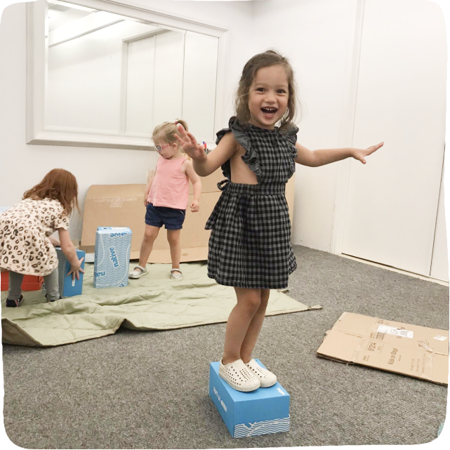 Little girl standing on a shoe box and laughing with her arms out wide