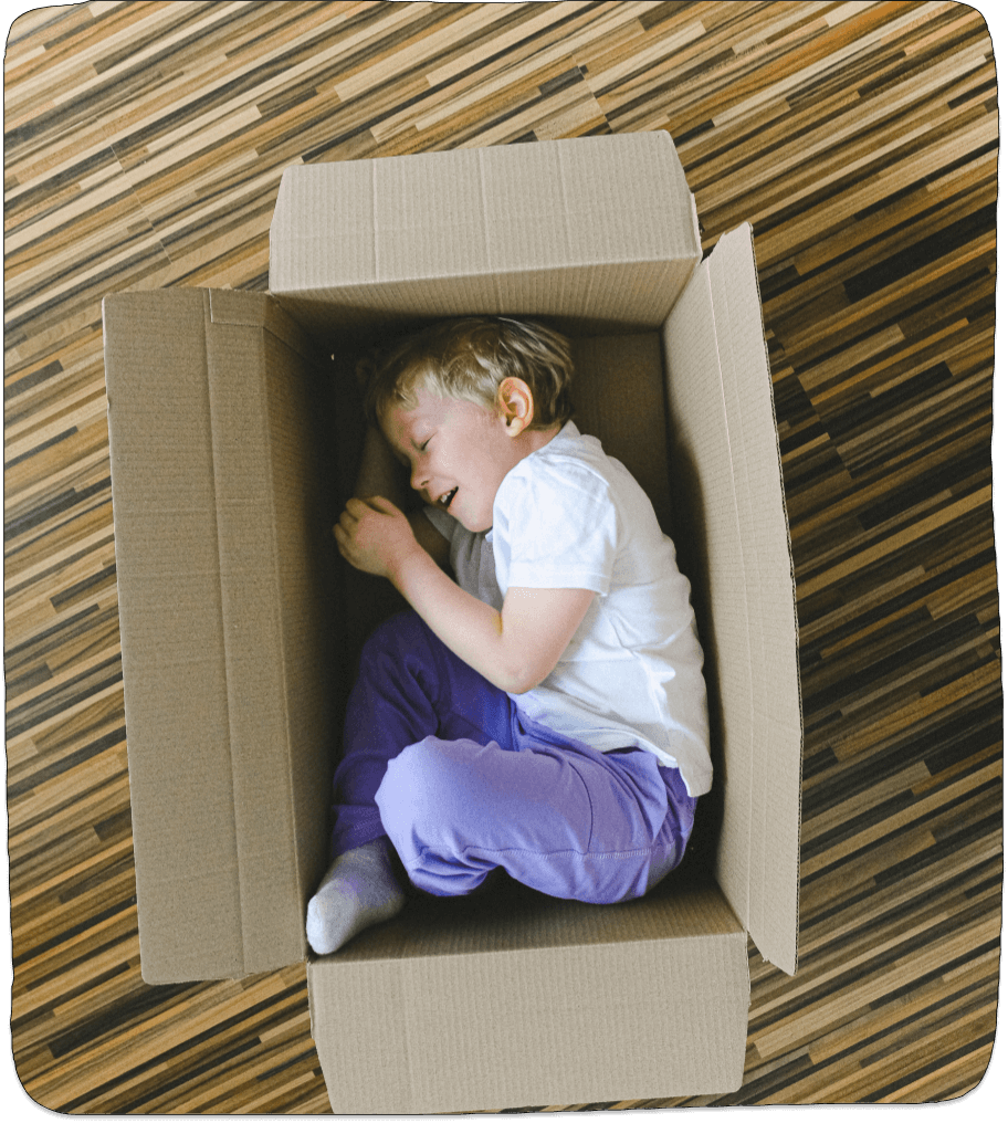 Little boy lying in a box all curled up to demonstrate the Value of cardboard box Play.