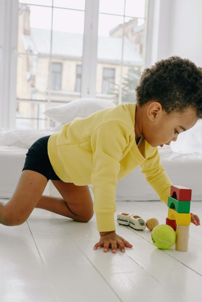 little boy playing on the floor with colorful wooden blocks and a tennis ball