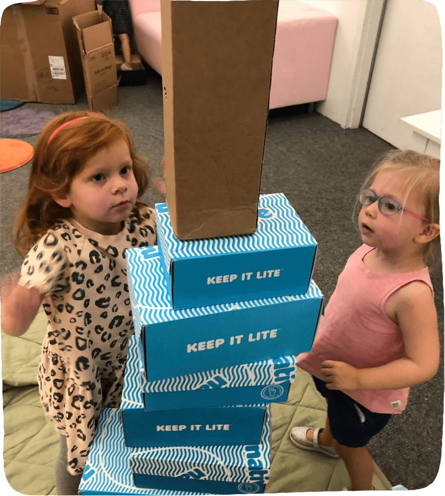 Two girls stacking a number of boxes into a tower.