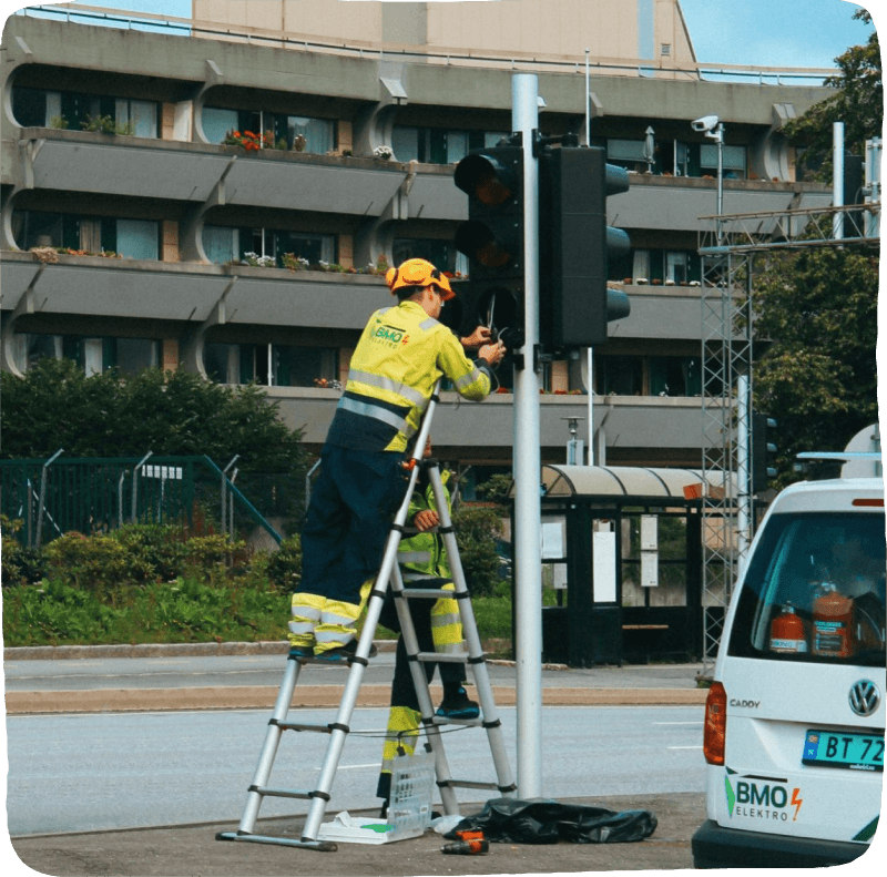 worker standing on a ladder, fixing a stop light on the street.