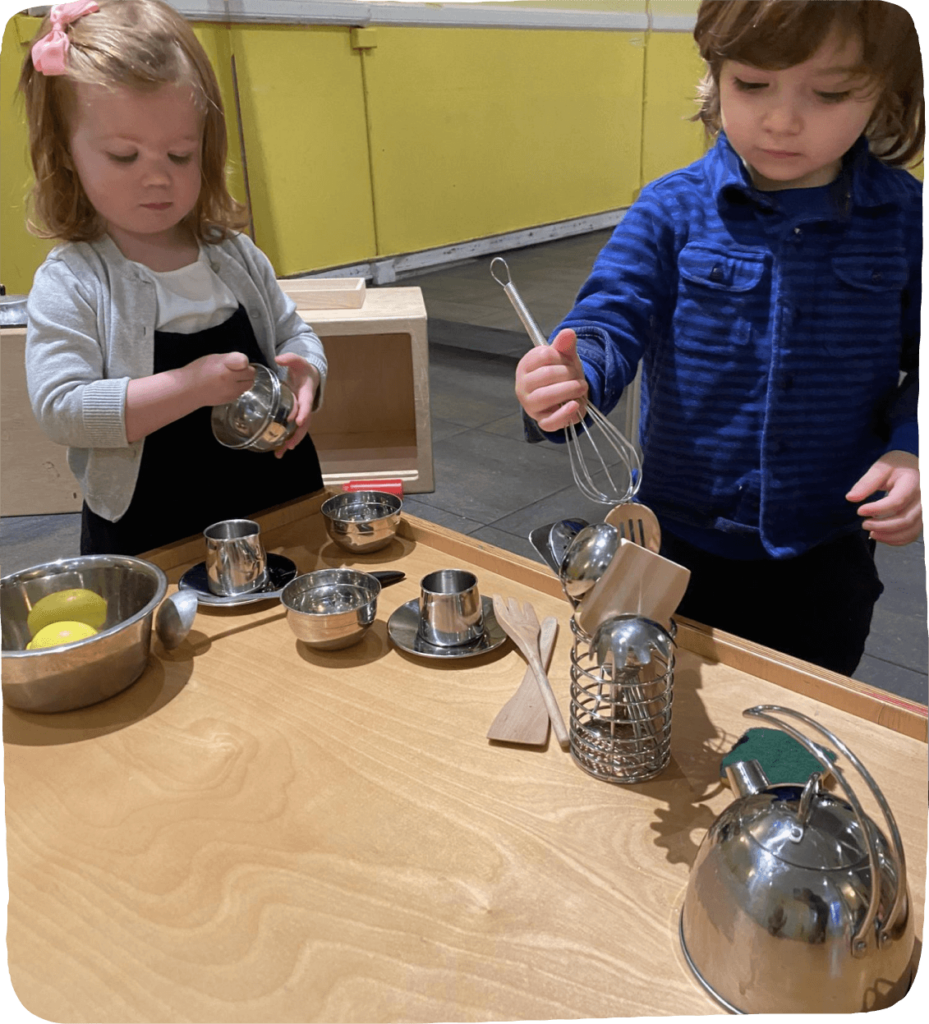 Image of two children engaging in a fun play activity by using pretend kitchen tools and pretending to cook.