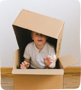 Boy sitting in one box with another box balanced over his head cardboard box.