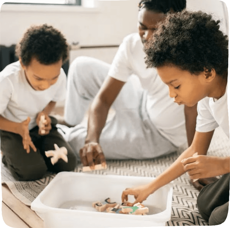 Two little boys and a father putting toys away in a bin for kids learning activities chores